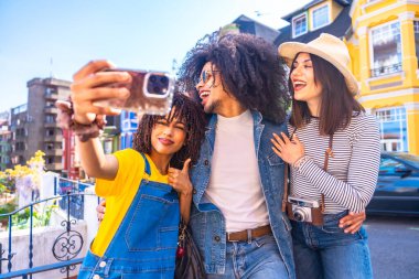 Bir grup mutlu turist Valparaiso, Şili 'deki renkli evlerin önünde akıllı telefonlarıyla selfie çekiyor ve yaz tatilinin tadını çıkarıyorlar.