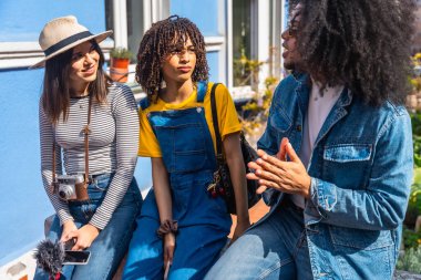 Üç genç içerik yaratıcısı video içeriği planlıyorlar sokakta oturmuş fikirleri tartışıyor ve paylaşıyorlar.