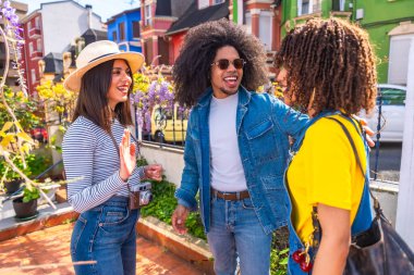 Üç mutlu turist, renkli evleri olan bir yerleşim bölgesinde birbirlerini selamlıyor ve tatillerinin tadını çıkarıyorlar.