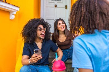 Üç neşeli arkadaş canlı bir sohbetin ve serinleticilerin keyfini çıkarırken canlı basamaklarda oturup neşeli ve sosyal bir atmosfer yaratıyorlar.