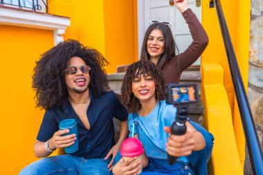 Üç mutlu çoklu etnik içerik yaratıcısı renkli adımlarla bir video blogu çekiyorlar.