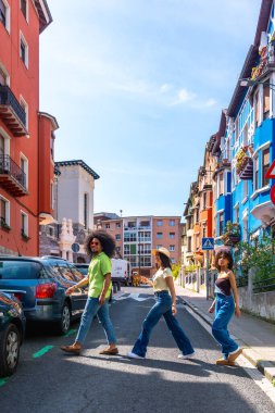 Üç turist canlı, renkli bir Avrupa kasabasında karşıdan karşıya geçiyor ve tatillerinin tadını çıkarıyorlar.