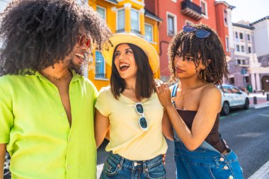 Üç farklı etnik gruptan genç arkadaş bir şehir caddesinde birlikte gülüyor ve yürüyorlar, tatillerinin tadını çıkarıyorlar.