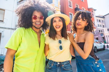 Üç neşeli genç arkadaş şehirde güneşli bir günün tadını çıkarıyorlar, neşeli yoldaşlıklarını kucaklıyorlar.