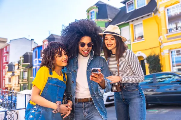 Üç genç turist, tatillerinde renkli bir caddede akıllı bir telefona danışarak seyahatlerinin tadını çıkarıyorlar.