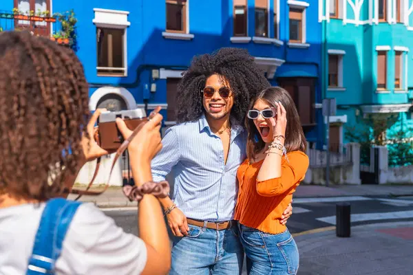 Genç turist, yaz tatilinde renkli bir sokakta poz veren sürpriz arkadaşlarının fotoğrafını çekiyor.
