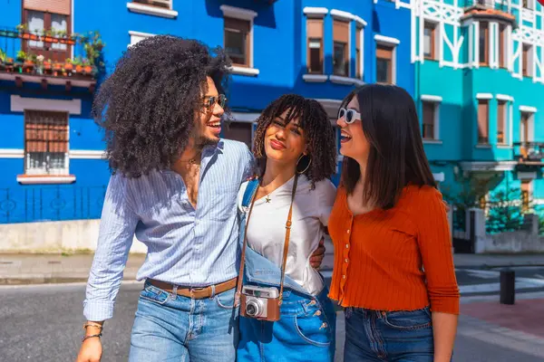 Renkli bir caddede yürüyen ve sohbet eden üç mutlu genç turist, tatillerinin tadını çıkarıyorlar.