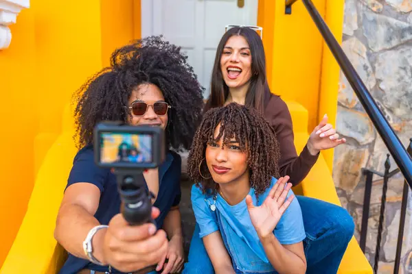 Canlı bir video blogunu renkli arka planlara sahip bir şehir ortamında çekerken kameraya el sallayan ve gülümseyen üç etkili kişi