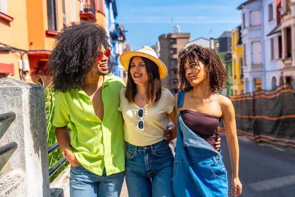 Üç mutlu çoklu etnik arkadaş güneşli bir günün tadını çıkarıyor. Bir şehir caddesinde birlikte yürüyüp gülüyorlar.