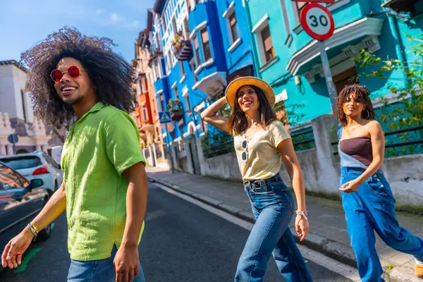 Bir grup şık, çok ırklı arkadaş yaz tatili boyunca renkli bir mahallede sokakta yürürken eğleniyorlar.