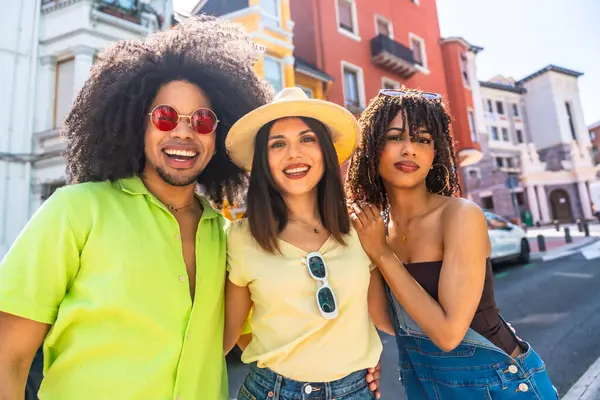 Üç neşeli genç arkadaş şehir merkezinde yürüyorlar, güneşli bir yaz gününün tadını çıkarıyorlar.