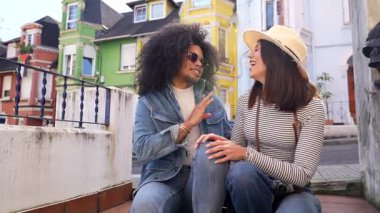 Üç mutlu turist, iki kadın ve bir erkek, renkli evlerin önünde oturup konuşuyorlar, tatillerinin tadını çıkarıyorlar.