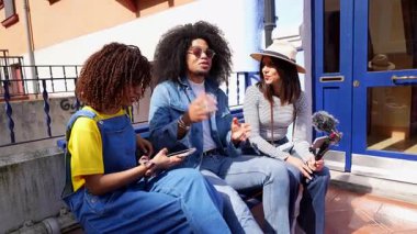 Genç içerik yaratıcıları video röportajında iş birliği yapıyor, mikrofon ve akıllı telefonla kayıt yapıyor, sokak bankında oturmuş, yaratıcı tartışmaları yakalıyorlar.
