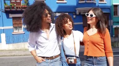 Neşeli genç turistler, güneşli yaz tatili sırasında canlı mavi şehir binasının yakınında poz verirken anılarını birleştiriyor ve yaratıyorlar.