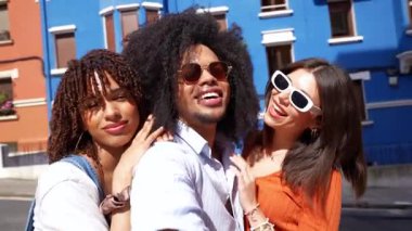 Bir grup neşeli çoklu etnik arkadaş, günlük kıyafetleriyle şehirde yürürken selfie çekiyorlar.