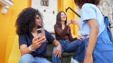 Çeşitli arkadaş grupları gülüyor, parlak sarı şehir duvarının yanında akıllı telefonlardan selfie çekiyor, gençlik bağlarının anlık görüntülerini yakalıyorlar.