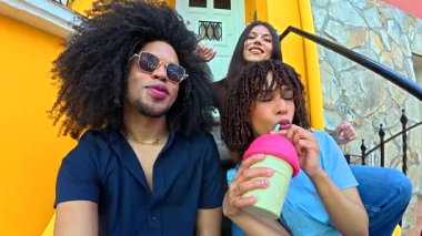 Farklı genç arkadaşlar renkli şehir merdivenlerinde neşeli selfie çekiyorlar, yaz tatilinde içkilerle keyifli anları paylaşıyorlar.