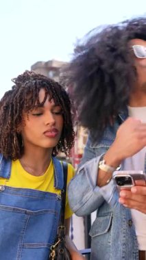 İki arkadaş, bir erkek ve bir kadın, şehirde yürüyüş yaparken akıllı telefon içeriğini paylaşıyor ve tartışıyorlar.