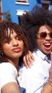 Bir grup farklı arkadaş güneşli bir günün tadını çıkarıyor, gülüyor ve canlı mavi bir binanın önünde birlikte anılar yaratıyorlar.