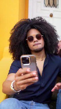 Arkadaşlar canlı ev basamaklarında birlikte poz verirken neşeli anları yakalıyorlar, şehir ortamında akıllı telefon kullanarak spontane selfie çekiyorlar.