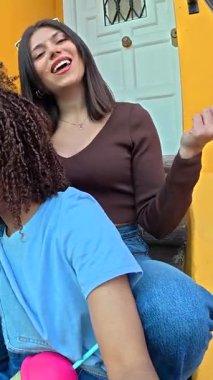 Bir grup neşeli genç arkadaş canlı sarı binaların basamaklarında gülüyor, konuşuyor ve içki içiyorlar.