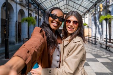 İki neşeli kadın gülümsüyor ve muhteşem bir cam ve metal çatı altında selfie çekiyor. Arkadaşlık ve macerayı birlikte kutluyorlar.
