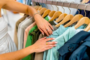 Mağazada elbise askısına bakan bir kadın, bir butikte alışveriş yaparken şık kıyafetler seçen bir kadın.