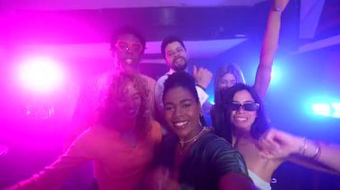 Neşeli çoklu etnik arkadaşlar bir gece kulübünde selfie çekiyorlar, müzik ve renkli ışıkların tadını çıkarıyorlar.