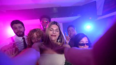 Çok kültürlü genç arkadaşlar enerjik parti sırasında renkli neon ışıkları altında selfie çekerken coşkulu bir gece kulübü anı yakalıyorlar, neşe ve heyecan paylaşıyorlar.