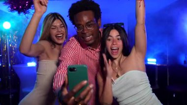 Enerjik arkadaşlar dans ederken ve kutlama yaparken selfie çekiyorlar. Canlı gece kulübü ışıkları ve titreşimli atmosfer arasında unutulmaz anlar yaratıyorlar.