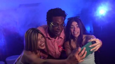 Arkadaşlar neşeli anları yakalar, enerjik gece klübü kutlamalarında canlı, renkli aydınlatma ve şenlikli atmosferle akıllı telefonlardan selfie çeker.