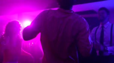 Genç yetişkinler arkadaşlığı, dansı ve kadeh kaldırmayı canlı, mor ışıklı gece kulübünde kutluyorlar.