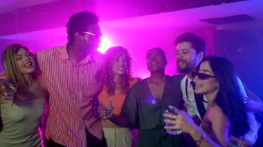 Kalabalık dans pistinde kaynaşan enerjik genç yetişkinler, yüksek sesli müzik eşliğinde canlı neon pembe ve mor kulüp ışıkları altında kokteylleri paylaşıyorlar.