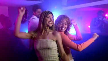 Enerjik bir şekilde müzikle hareket eden, neşeyle dans eden ve birlikte heyecan verici gece kulübü anlarını paylaşan, kaygısız mutluluğu ve canlı bağlantıyı ifade eden bayan arkadaşlar.