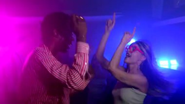 Genç yetişkinlerin enerjik bir şekilde müziğe yöneldiği canlı bir gece kulübü sahnesi. Renkli sahne ışıkları altında arkadaşlığı ve neşeli hafta sonu gecesini kutluyoruz.