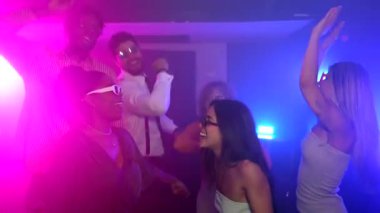 Canlı pembe ve mavi ışıkları olan bir gece kulübünde dans eden ve eğlenen enerjik arkadaşlar.
