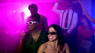 Genç kadınlar, neon ışıklarının arasında arkadaşlarıyla dans ederek neşe ve gençlik kültürünün kutlamalarıyla dolu enerjik bir gece kulübü atmosferi yaratıyorlar.