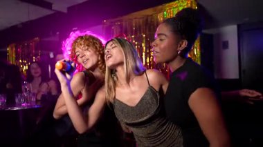 Dişi arkadaşlar coşkuyla mikrofonlara şarkı söylüyor, kızlar gecesi canlı gece kulüplerinde neşeli karaoke anlarını paylaşıyorlar.