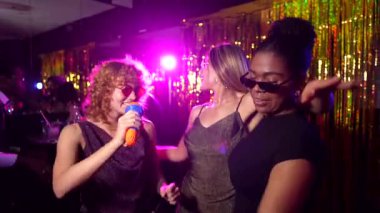 Neşeli bayan arkadaşlar mikrofonlara tutkuyla şarkı söylüyor, canlı bir barda enerjik bir karaoke performansı paylaşıyorlar bulaşıcı bir heyecan ve dostluk dolu bir gece geçiriyorlar.