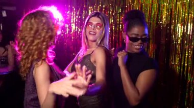 Çoklu etnik bayan arkadaşlar dans ediyor ve hareketli bir gece kulübü atmosferinin tadını çıkarıyor. Arkadaşlık ve kutlama dolu anları paylaşıyorlar.