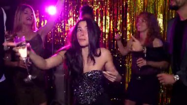 Genç yetişkinler dans ediyor ve canlı bir partide içkinin tadını çıkarıyorlar altın arka planı ve mor ışıklarıyla