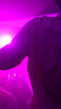 Gece kulübü kalabalığı enerjik bir şekilde dans ediyor, mor ışıklar altında kokteyller kaldırıyor, hafta sonu gece hayatını bulaşıcı bir neşe ve gençlik heyecanıyla kutluyorlar.