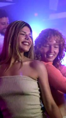 Kadın arkadaşlar enerjik bir şekilde dans ediyorlar, vücutlarını elektronik müzik eşliğinde gece kulübü atmosferine taşıyorlar, enerjik gece hayatı enerjisini ve gençlik neşesini somutlaştırıyorlar.