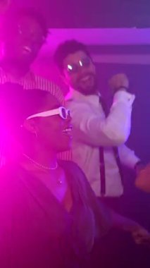 Genç yetişkinlerin enerjik bir şekilde dans ettiği canlı bir gece kulübü sahnesi, elektronik müziğe geçiş, kalabalık dans pistinde coşku ve heyecanı lazer ışıkları ve dinamik atmosferle paylaşmak.