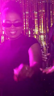 Şampanyayla kutlama yapan, dans eden ve ışıldayan altın arkaplan karşısında gülen büyüleyici kadınlar.