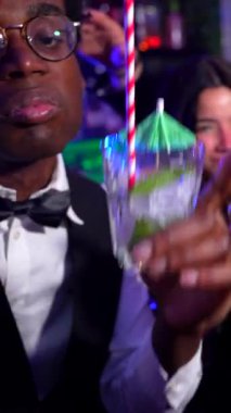 Arkadaşlar kokteyl bardaklarını tokuşturuyor, enerjik gece kulübü ortamında kahkaha ve neşe paylaşıyorlar, çeşitli gruplar arasındaki bağlantıyı kutluyorlar.