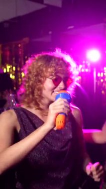 Genç bayan arkadaşlar yüksek enerjili karaoke gecelerinin keyfini çıkarıyorlar, yerel gece kulübünde canlı müzik ve neşeli enerjiyle birlikte dans ediyorlar.
