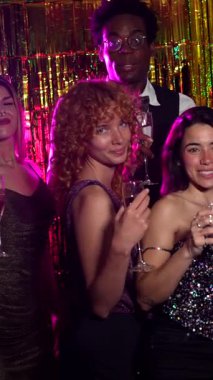 Gösterişli bir partide ellerinde şampanya bardaklarıyla poz verip gülümseyen şık arkadaşlar.