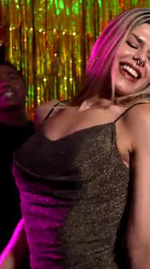 Canlı bir grup arkadaş dans ediyor, şarkı söylüyor ve renkli ışıklar ve müzikle gece hayatı enerjisini kutluyorlar.