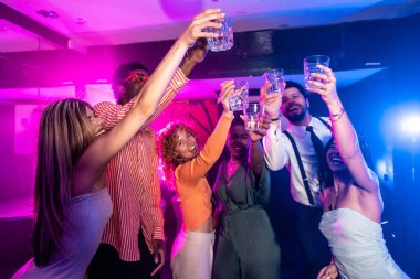 Mutlu çoklu etnik arkadaşlar kadeh kaldırıyor, gece hayatının tadını çıkarıyor ve gece kulübü partisinde birlikte kadeh kaldırıyoruz.